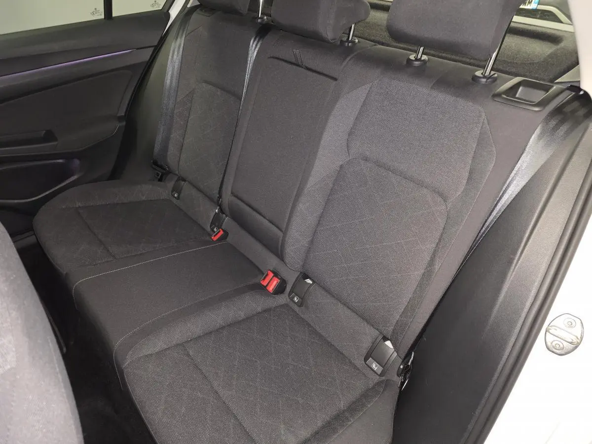 Vue intérieure côté droit de la banquette arrière tissu gris foncé de la Volkswagen Golf VIII blanche, avec ceintures de sécurité visibles.