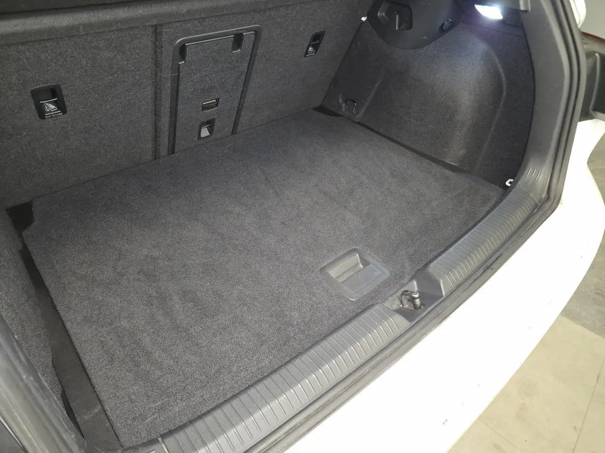 Coffre ouvert d’une Volkswagen Golf VIII blanche, montrant le tapis de sol et l’éclairage intérieur du coffre.