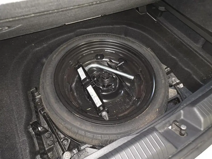 Gros plan sur la roue de secours noire et le cric dans le coffre d'une Volkswagen Golf VIII blanche.