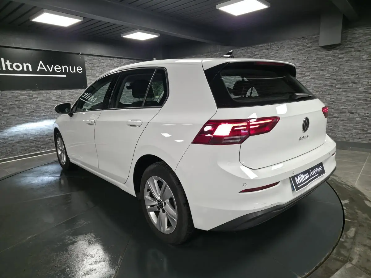 Volkswagen Golf VIII blanche vue 3/4 arrière droit en intérieur avec feux arrière allumés.