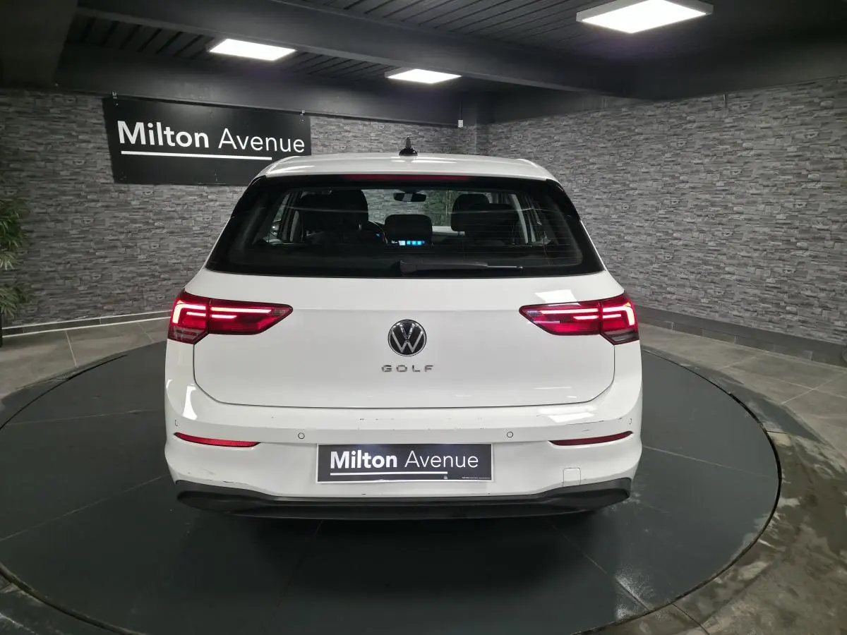 Vue arrière d'une Volkswagen Golf VIII blanche avec feux arrière LED allumés dans un showroom.