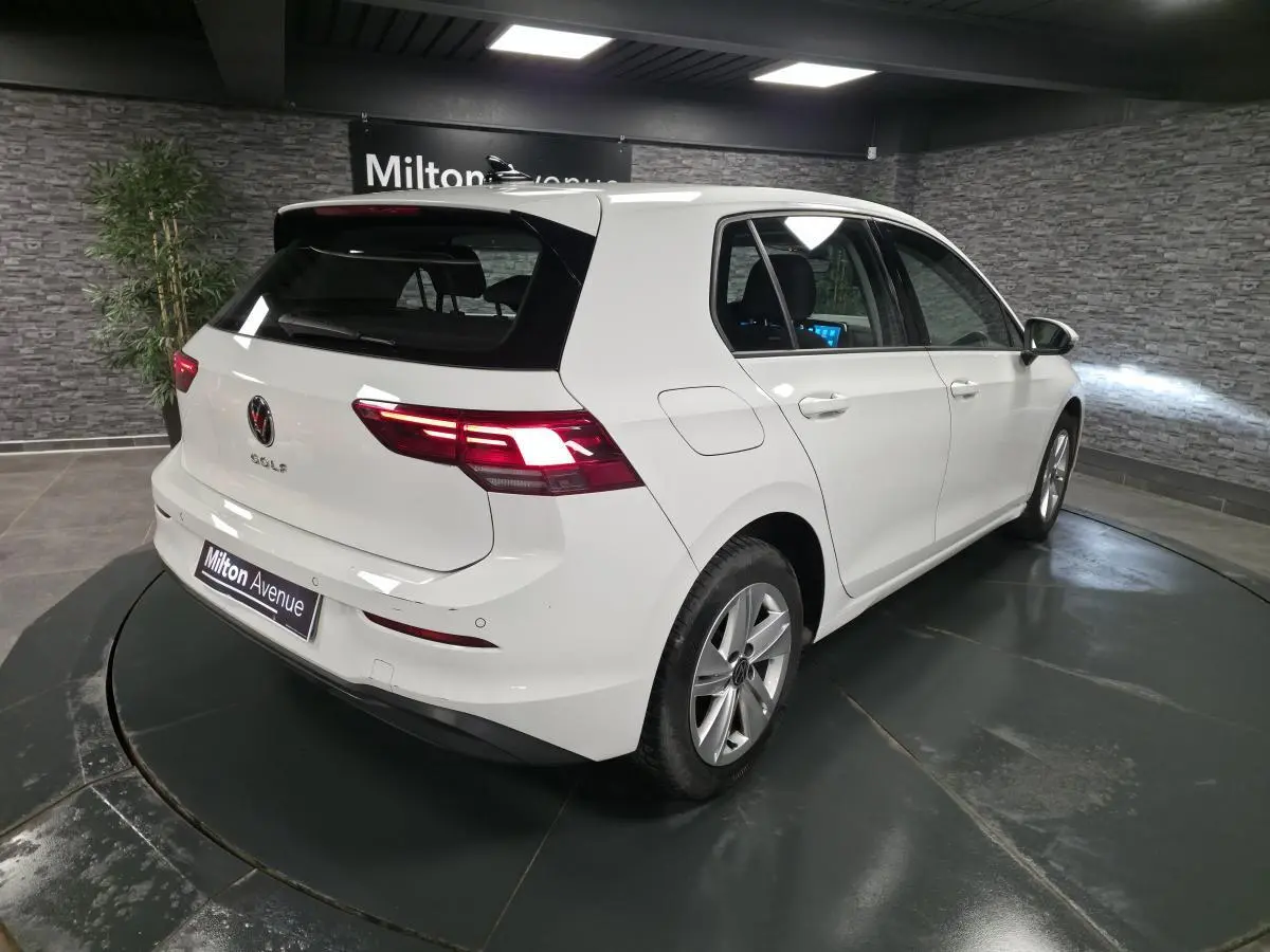 Volkswagen Golf VIII blanche vue 3/4 arrière droit en intérieur avec feux arrière LED allumés.