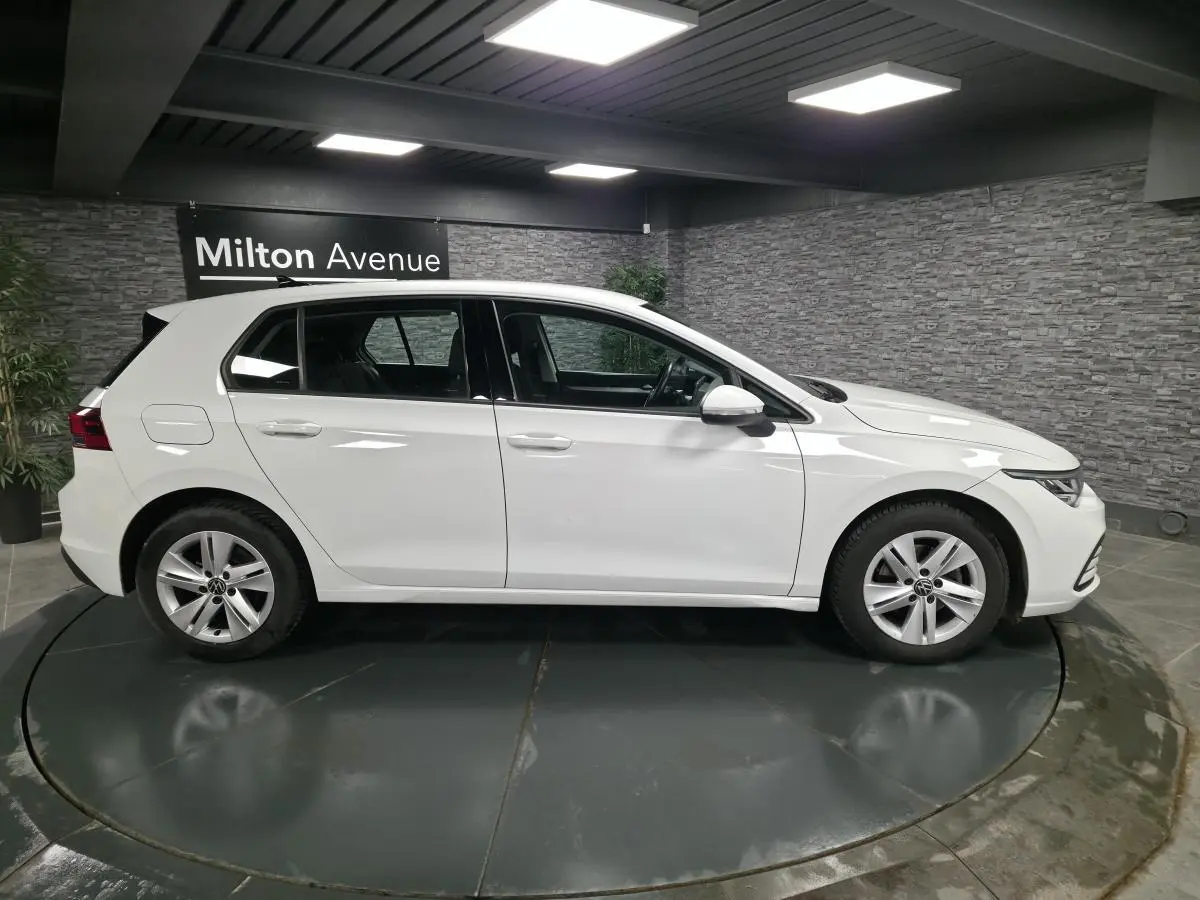 Profil côté gauche d'une Volkswagen Golf VIII blanche, en intérieur avec jantes alliage et éclairage LED au plafond.