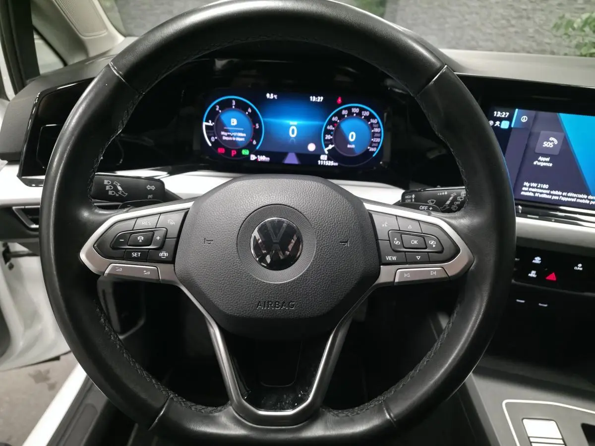 Vue rapprochée du volant noir multifonction et du tableau de bord digital lumineux d'une Volkswagen Golf VIII blanche.