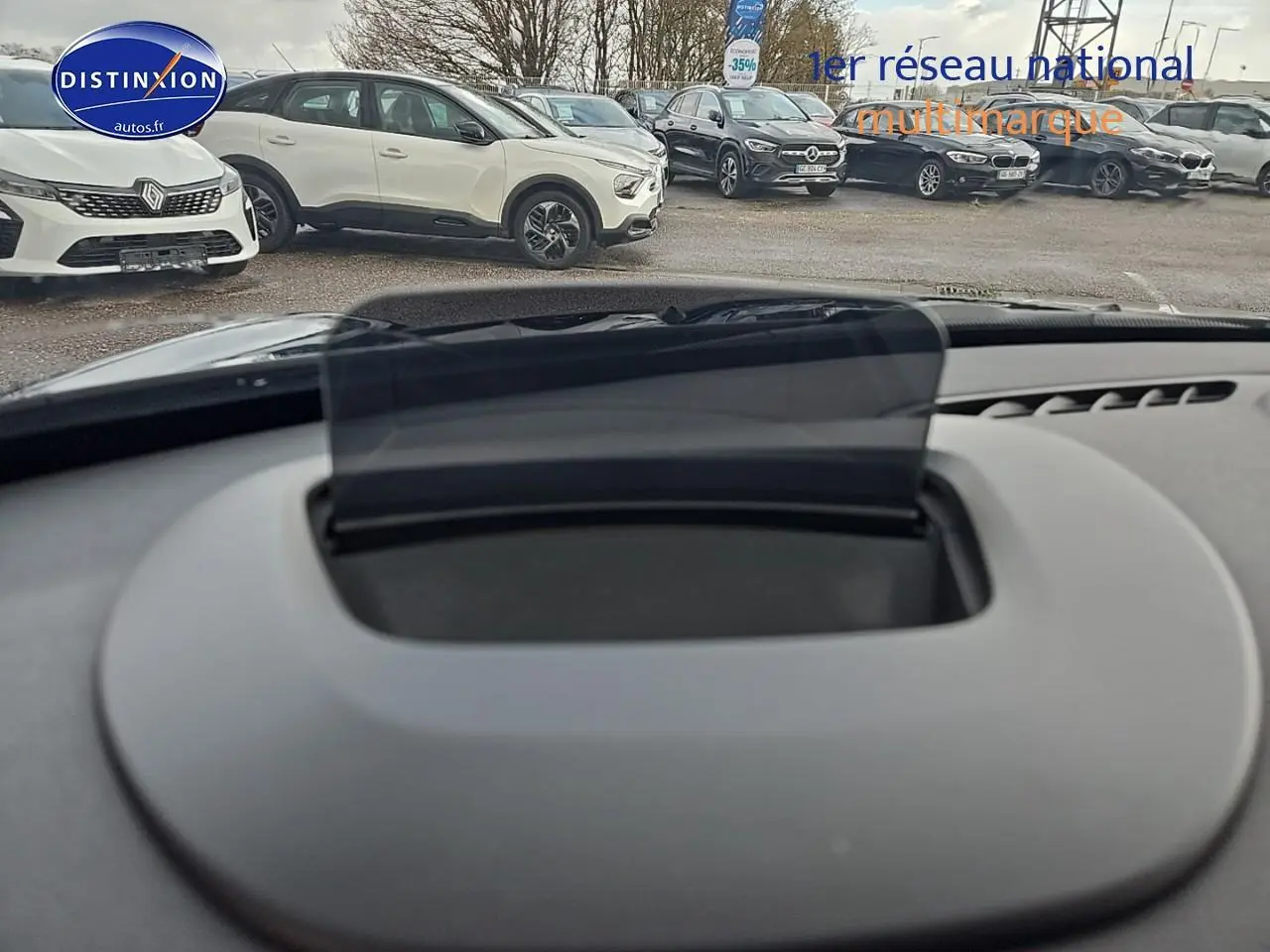 Vue intérieure du tableau de bord de la MINI Cooper S 2015 avec écran tête haute déployé, arrière-plan extérieur flou.