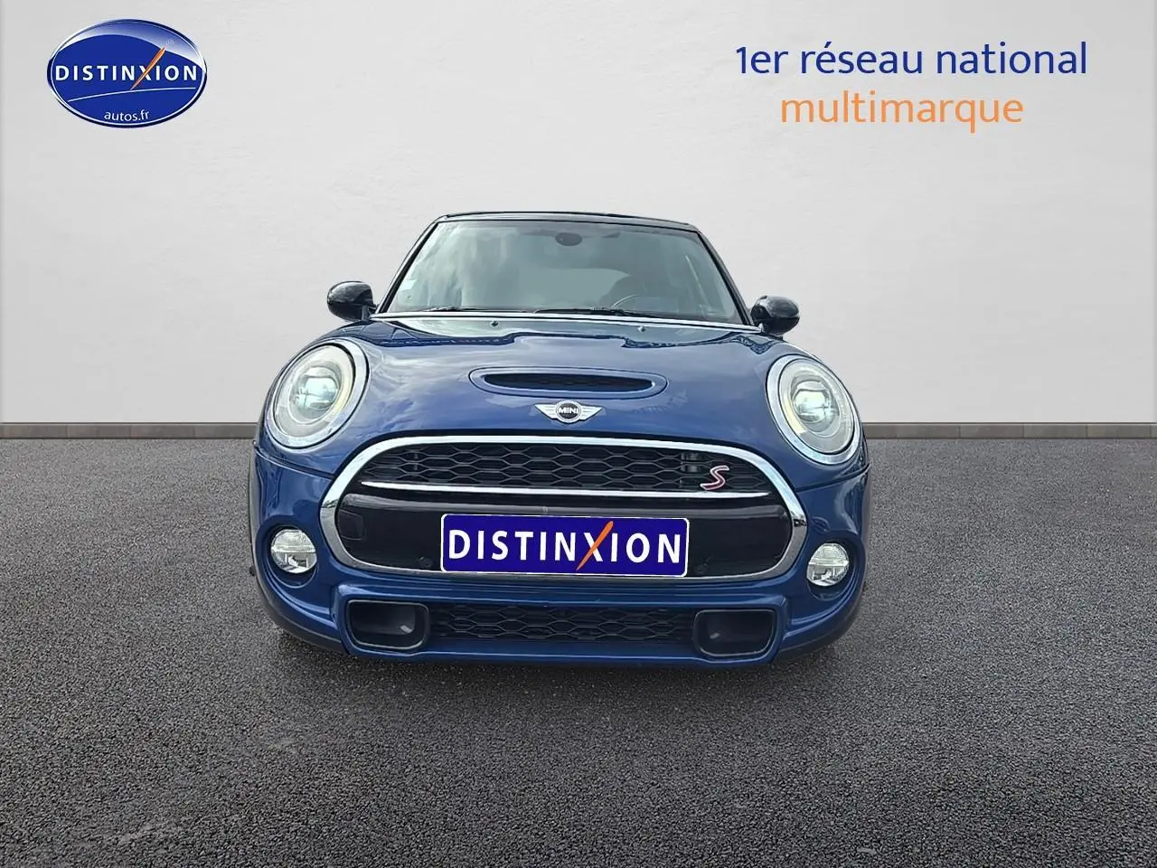 Vue frontale d'une MINI Cooper S bleu nuit avec calandre noire et détails chromés, phares ronds allumés.