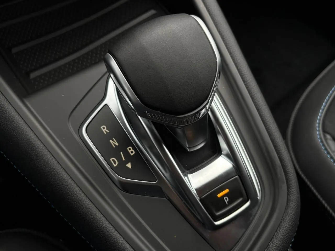 Gros plan sur le levier de vitesses automatique noir et chrome du Renault Captur hybride, avec bouton de parking éclairé.