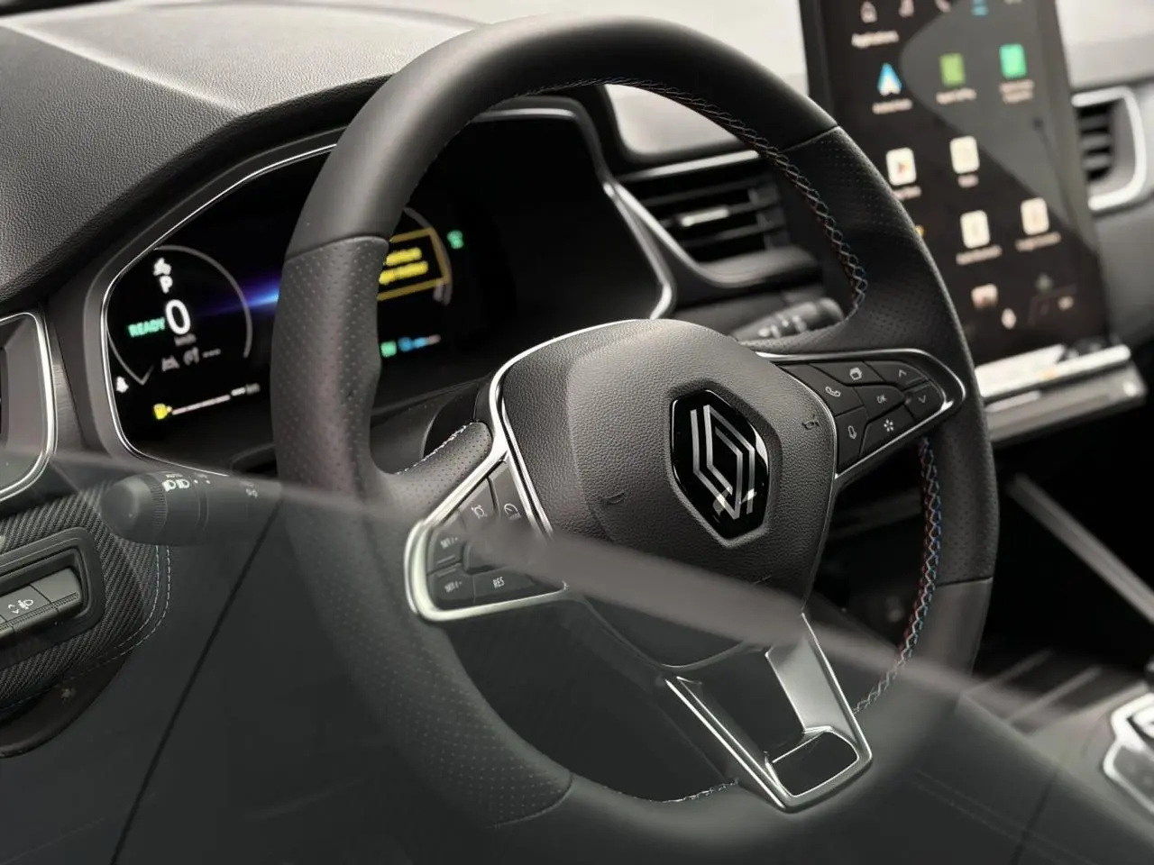 Gros plan sur le volant noir avec surpiqûres tricolores du Renault Captur 2025, tableau de bord numérique en arrière-plan.