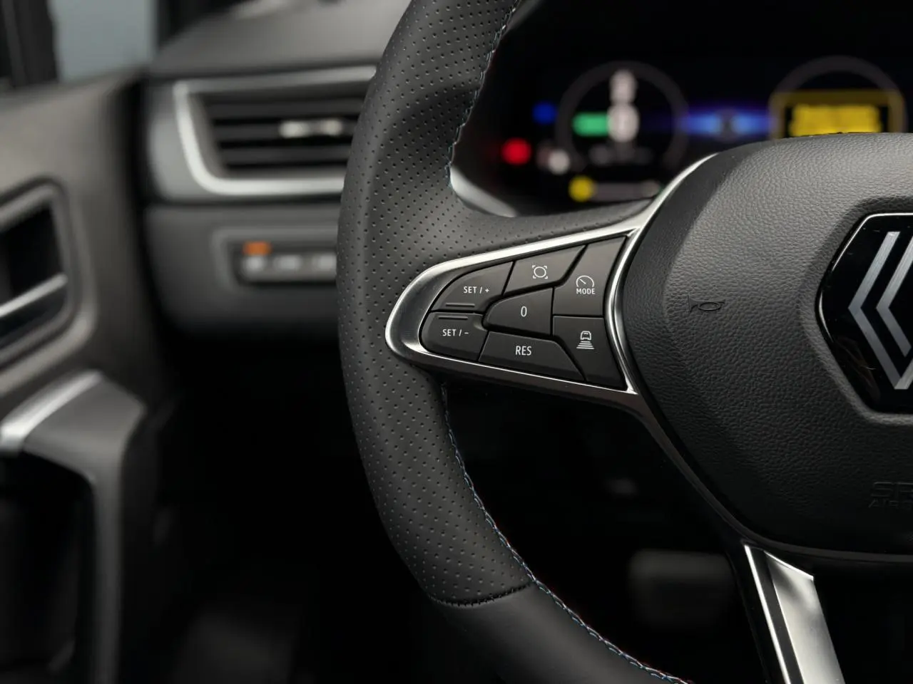 Gros plan sur le volant noir perforé avec surpiqûres tricolores du Renault Captur Esprit Alpine 2025, boutons de régulateur.