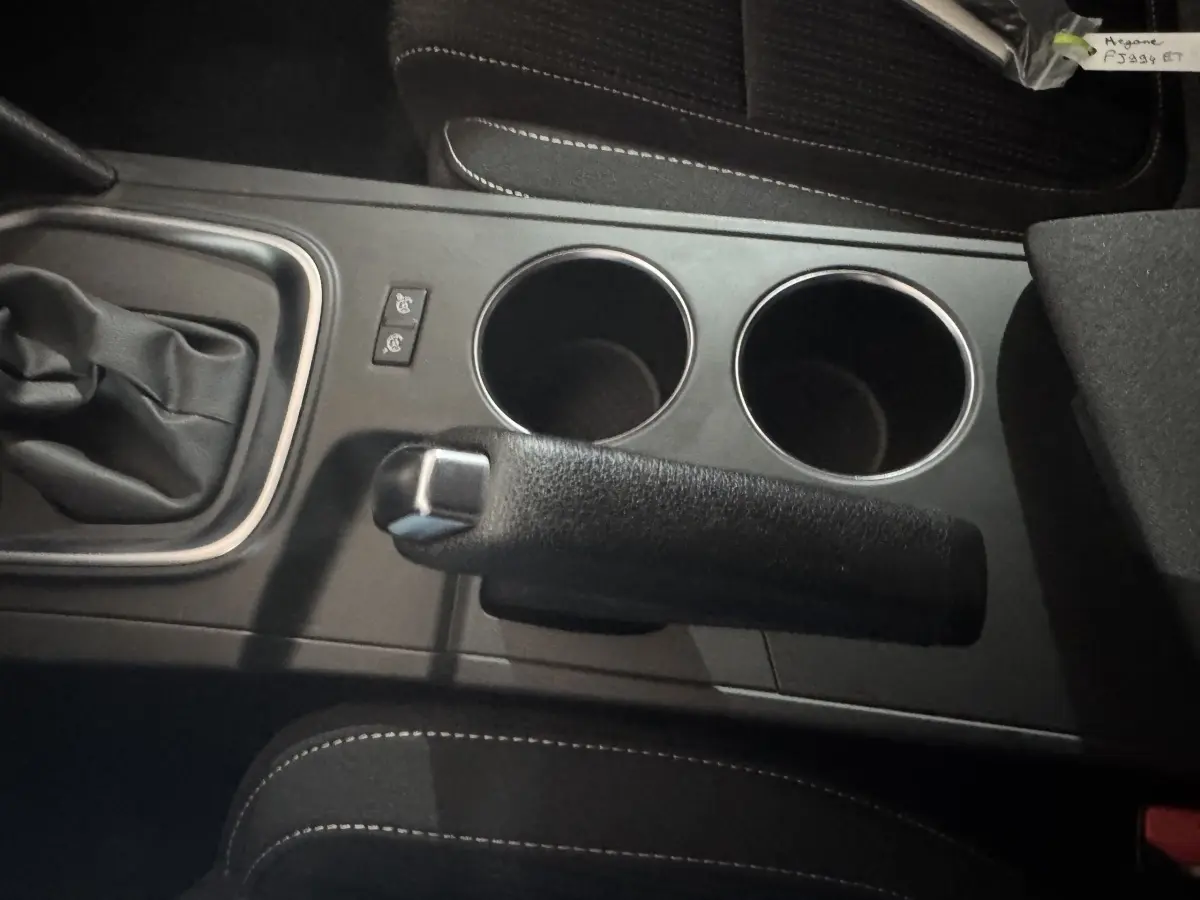 Vue rapprochée de la console centrale noire avec frein à main, deux porte-gobelets et levier de vitesse d’une Renault Mégane Business gris clair.