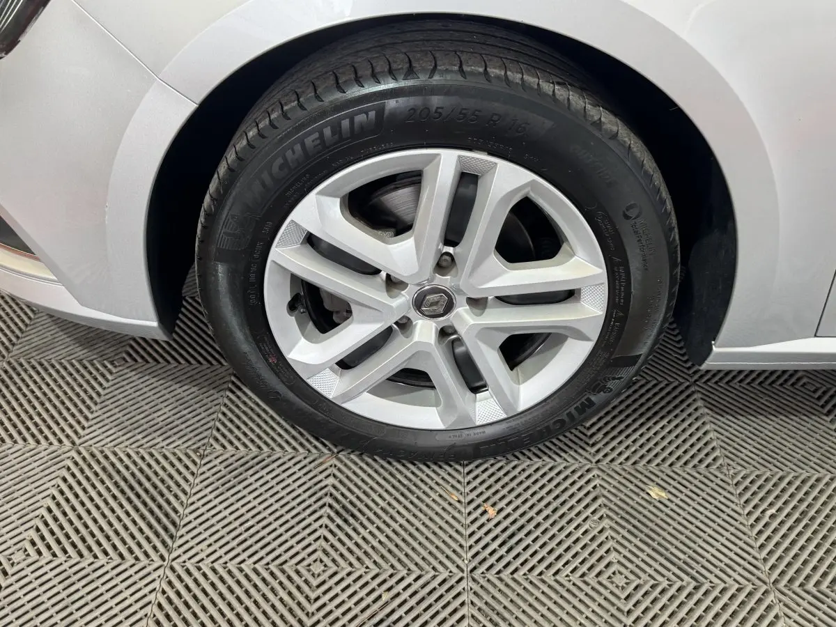 Vue rapprochée de la roue arrière droite d'une Renault Mégane Business gris clair sur sol texturé.