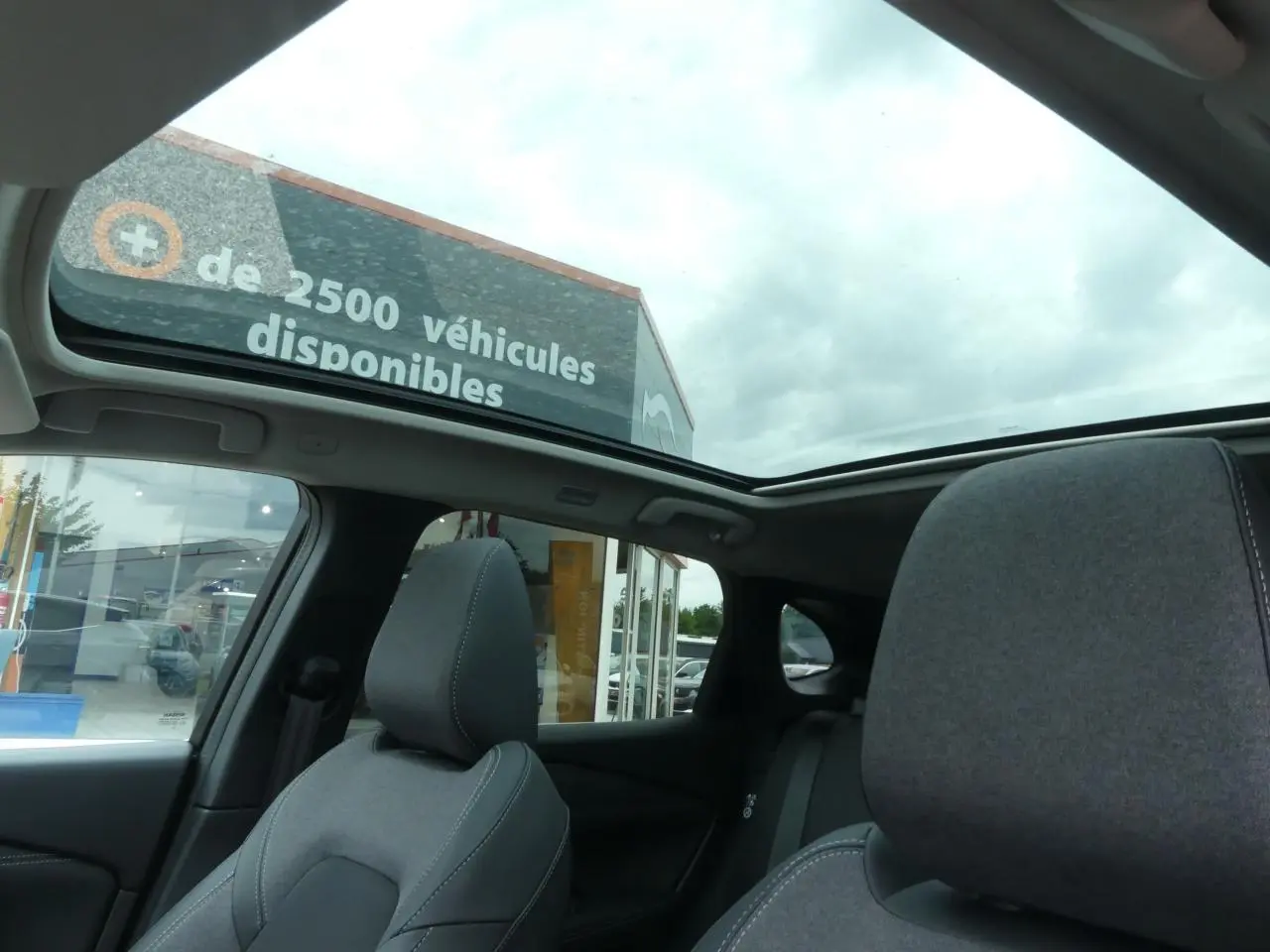 Vue intérieure du Nissan Qashqai 2025 gris, mettant en valeur le toit panoramique en verre et les sièges avant en tissu gris.