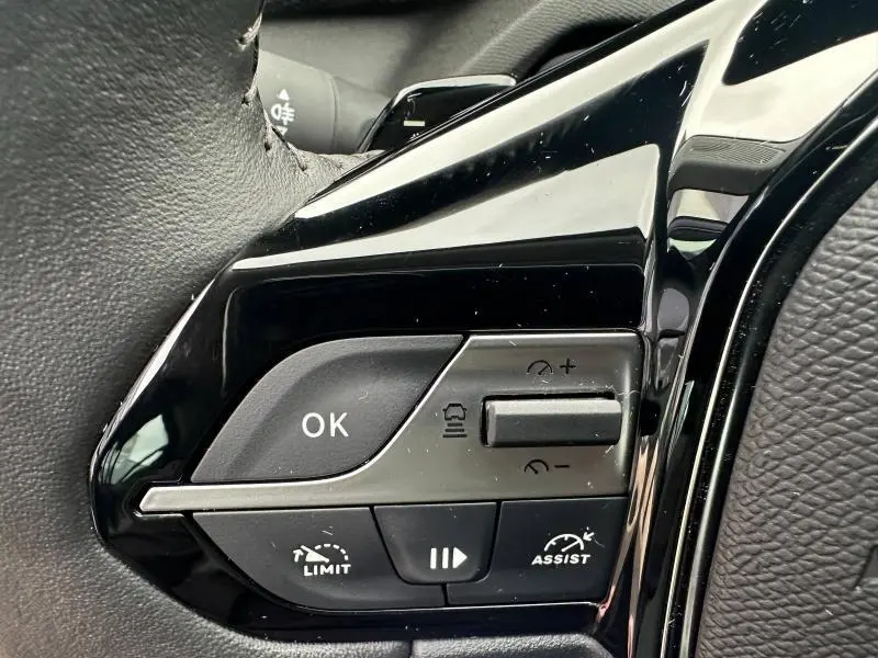Gros plan sur les commandes au volant noir brillant de la Peugeot 308 2024, version essence Noir Perla Nera.