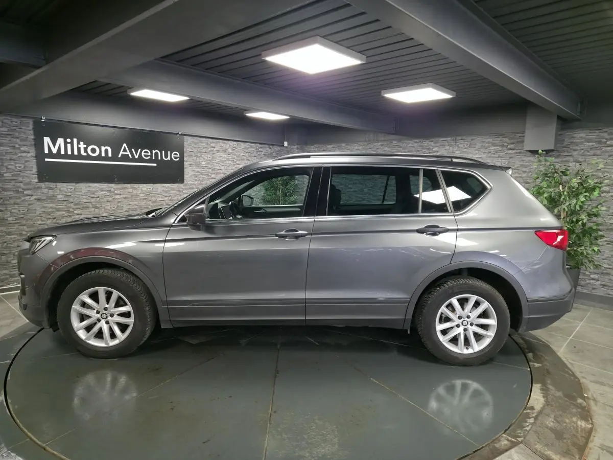 Vue de profil côté gauche d’un SEAT Tarraco gris, SUV 7 places avec jantes alliage 17 pouces dans un showroom.