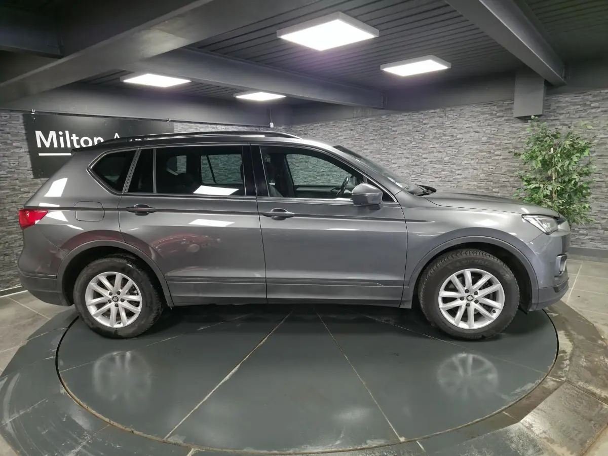Vue de profil côté gauche d'un SEAT Tarraco gris, SUV 7 places, sur jantes alliage 17 pouces dans un showroom.