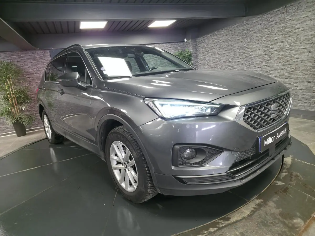 SEAT Tarraco gris en 3/4 avant droit, avec phares LED allumés et jantes alliage 17 pouces visibles.