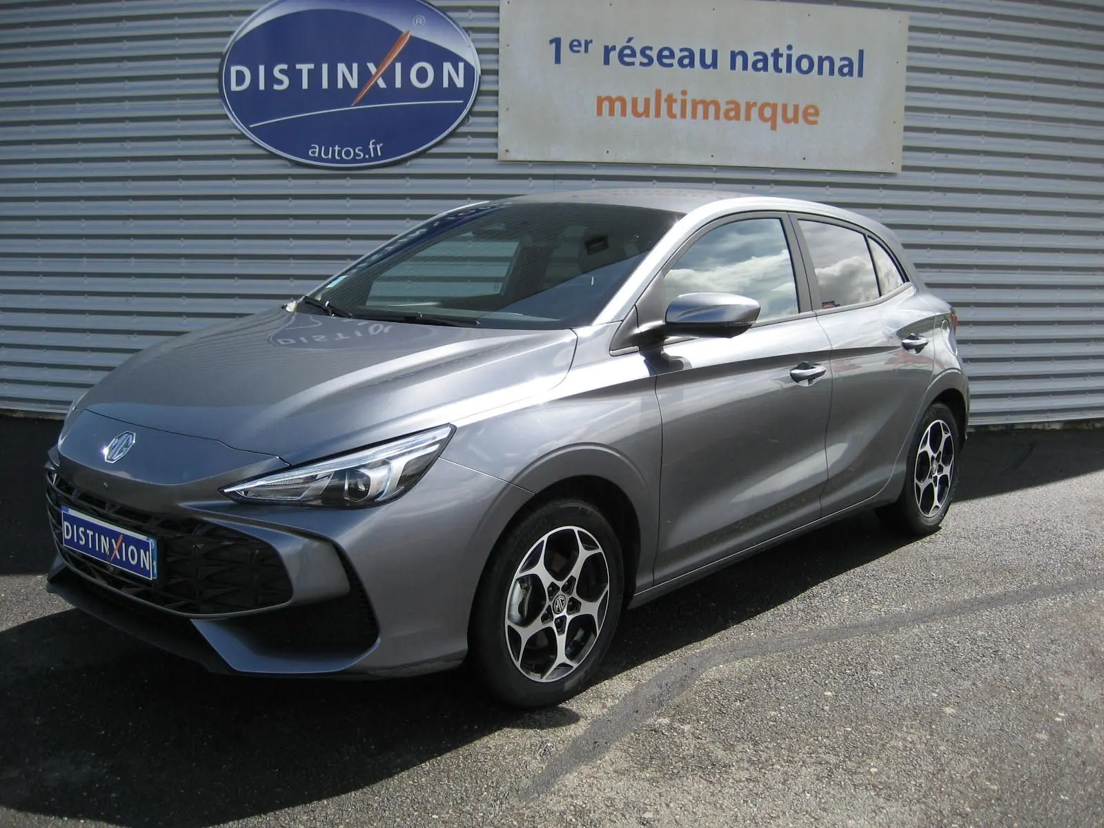 Vue 3/4 avant droite d'une MG3 gris métallisé 2025 avec jantes alliage et calandre noire distinctive.