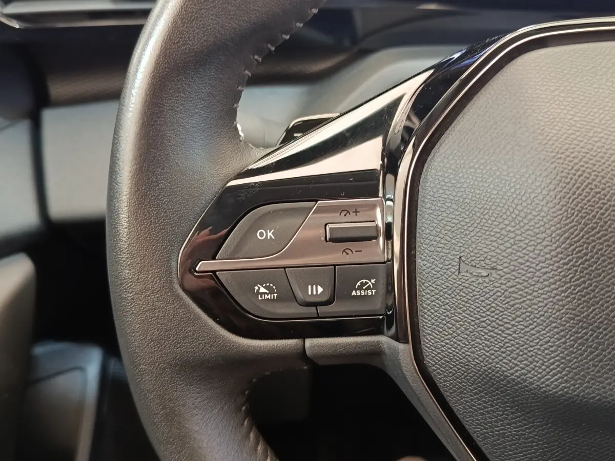 Gros plan sur le côté gauche du volant cuir noir de la Peugeot 308 avec commandes multifonctions visibles.