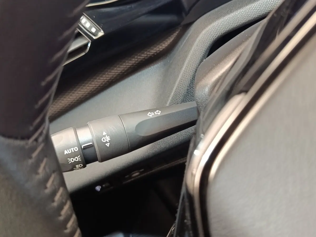 Gros plan sur la manette de clignotants et commandes d’éclairage côté gauche du volant cuir d’une Peugeot 308 verte.