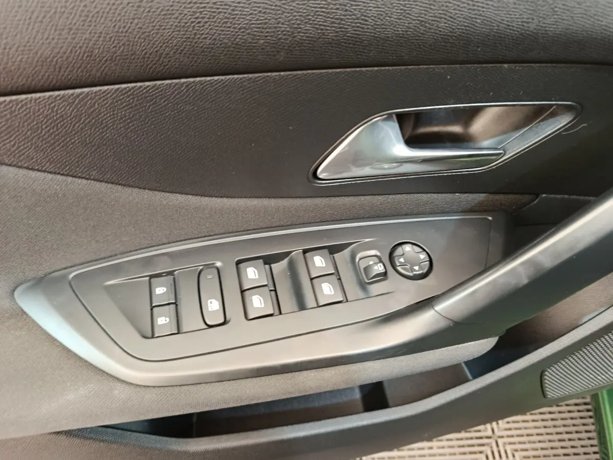 Détail des commandes de lève-vitres et rétroviseurs sur la porte côté conducteur d’une Peugeot 308 vert 2023.