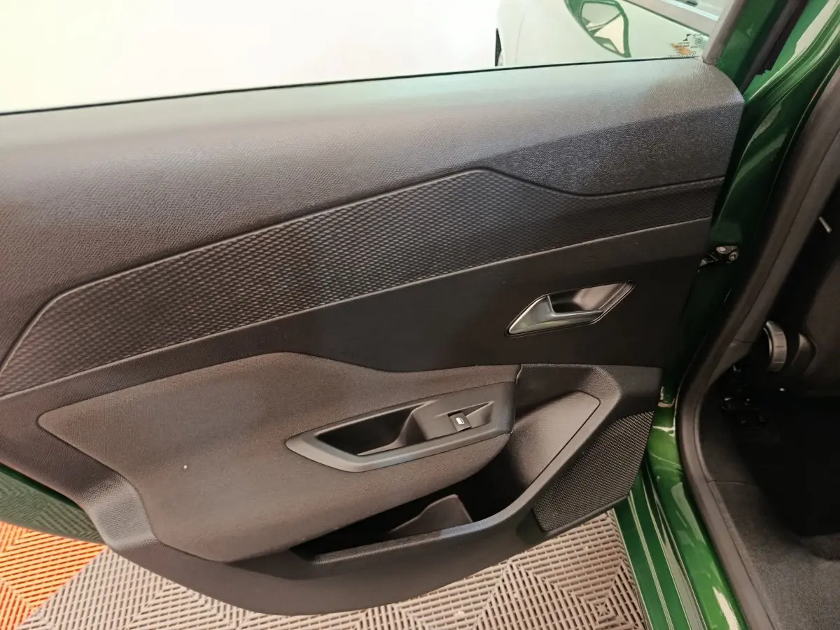 Vue intérieure sur la porte arrière gauche d'une Peugeot 308 2023 vert avec commandes de vitre et haut-parleur intégré.