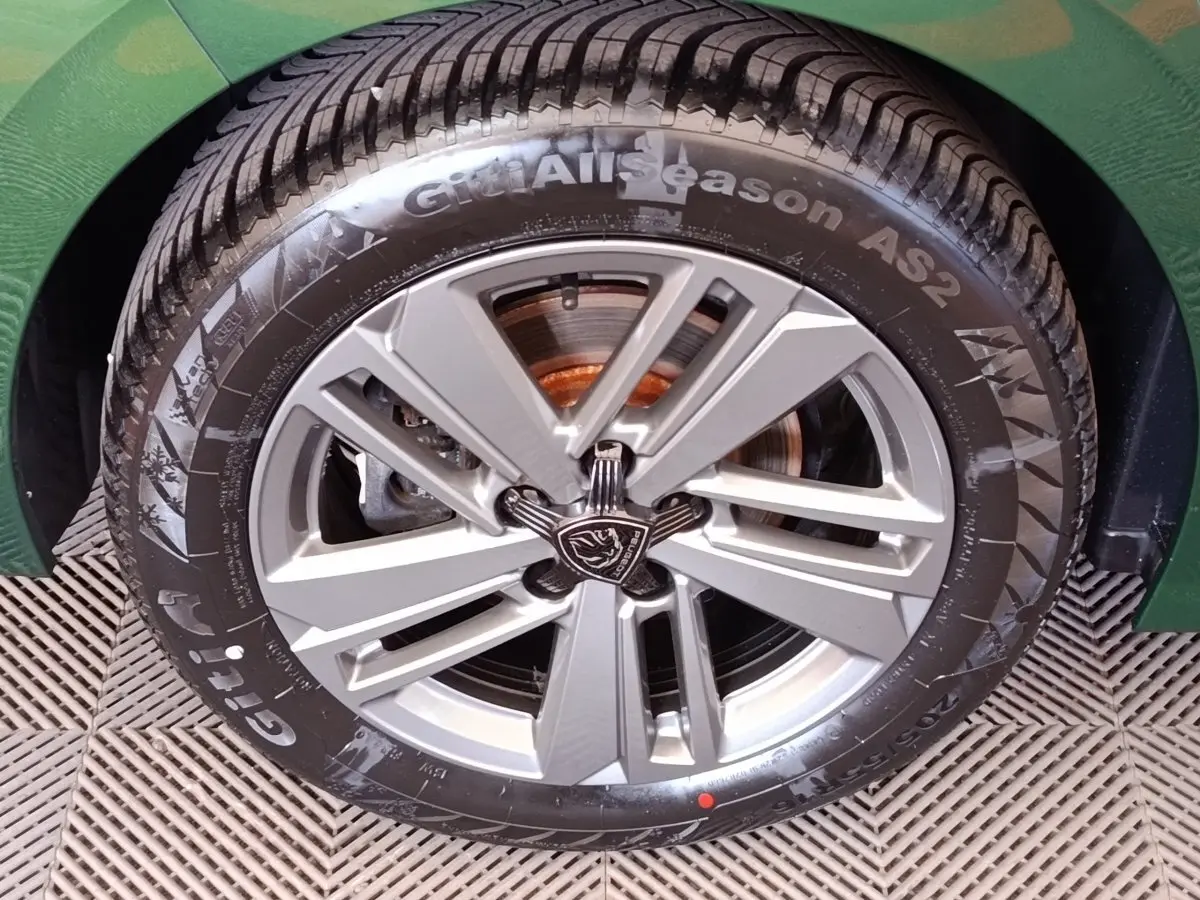 Gros plan sur la roue avant droite d'une Peugeot 308 vert 2023, mettant en valeur la jante alliage et le pneu toutes saisons.