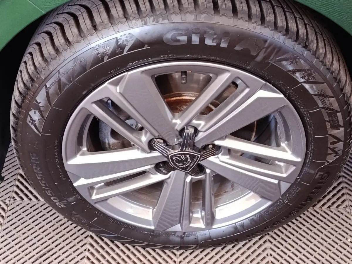 Gros plan sur la roue avant droite d'une Peugeot 308 verte, jante alliage à design moderne et logo lion central.