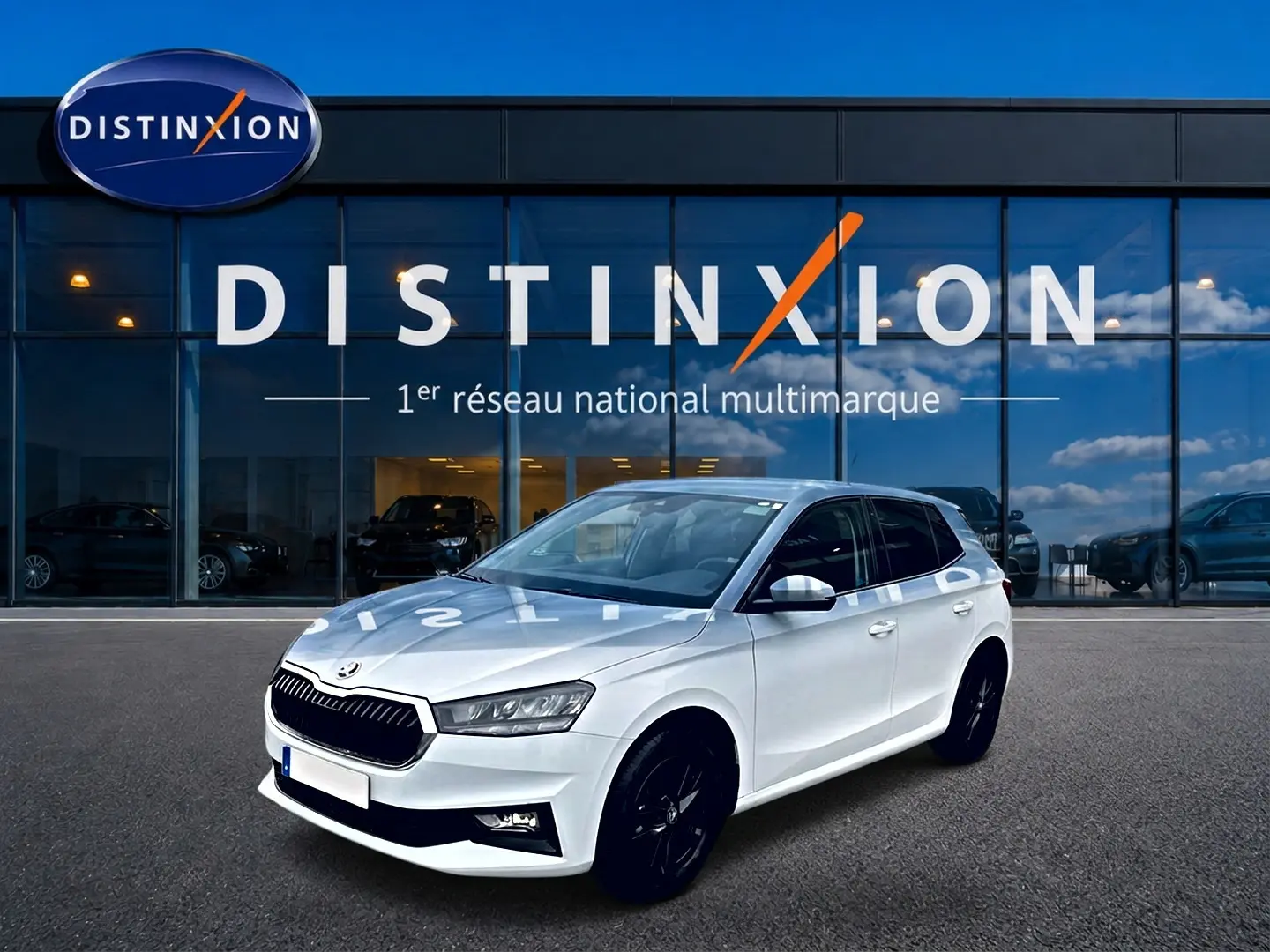 SKODA FABIA blanche vue en 3/4 avant droit, avec jantes noires et calandre distinctive devant un showroom Distinxion.