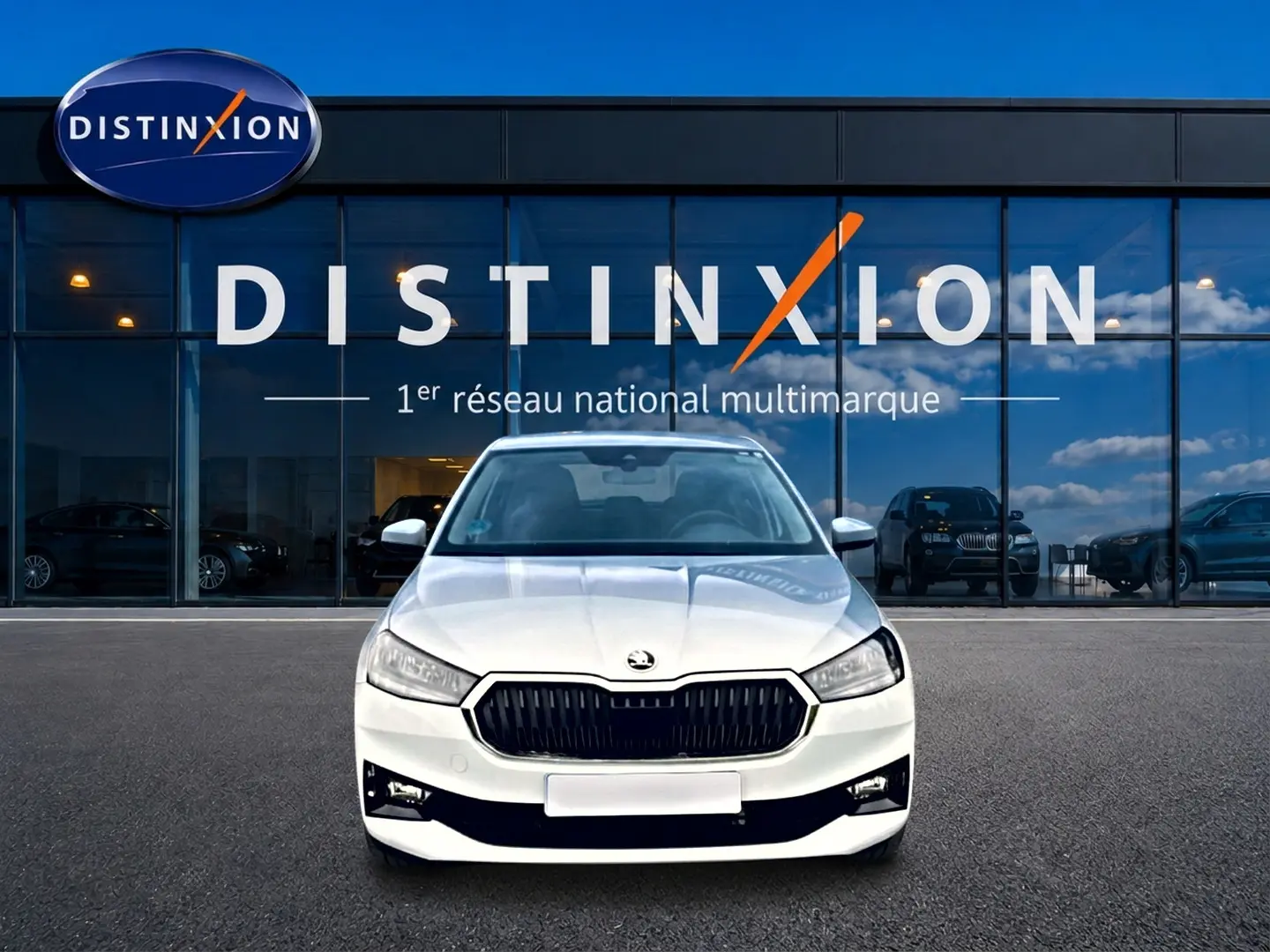Vue avant d'une Skoda Fabia blanche 2025 avec calandre noire, garée devant une vitrine Distinxion.