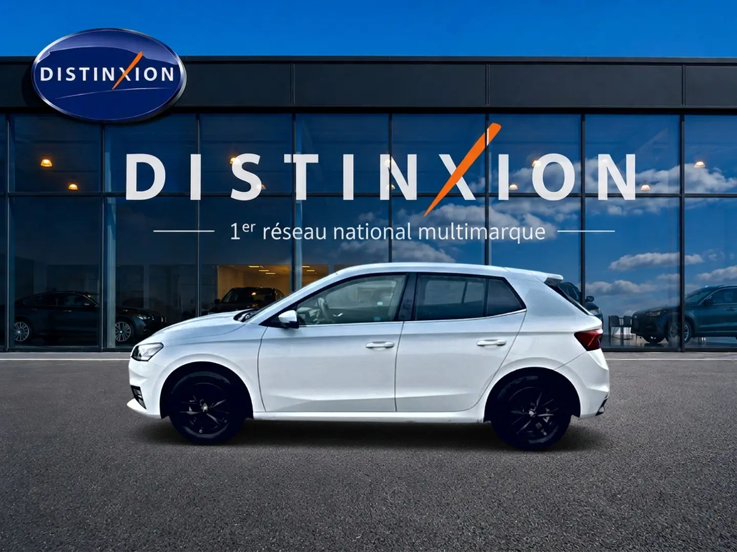Vue latérale droite d'une Skoda Fabia blanche 2025 avec jantes noires, stationnée devant une vitrine Distinxion.