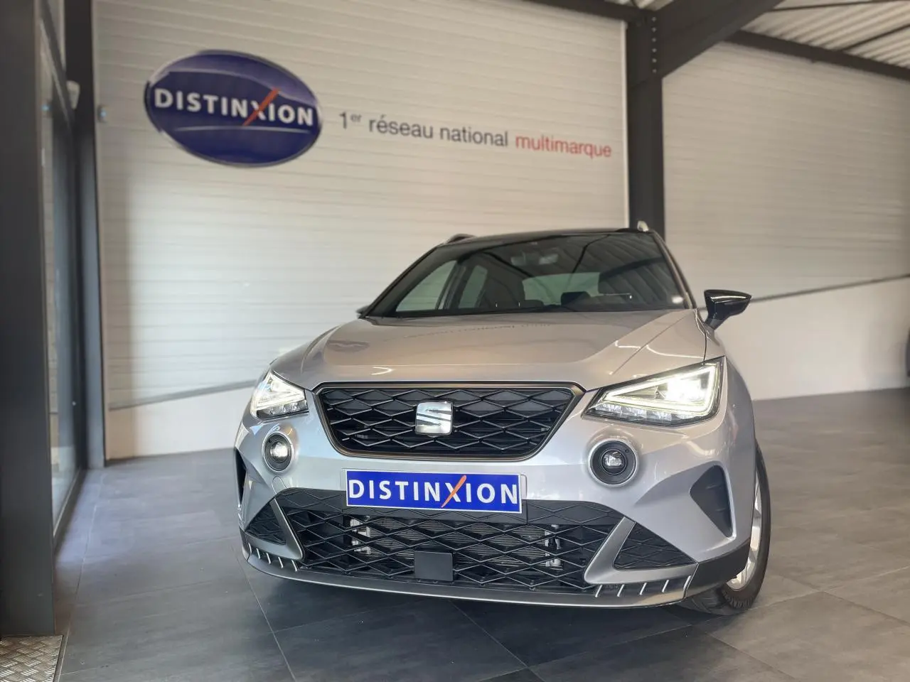 Vue de face d'une SEAT Arona 2024 gris GRS avec phares EcoLED allumés dans un showroom.