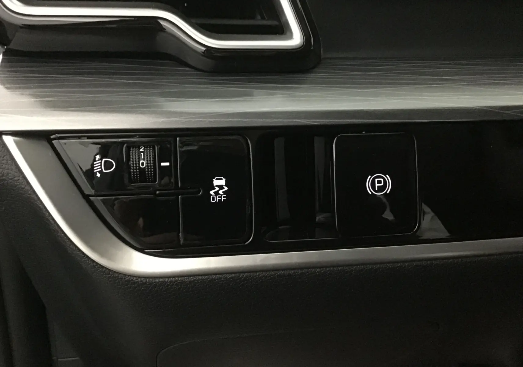 Gros plan sur les commandes de tableau de bord noir du Kia Sportage 2025, avec réglage des phares et frein à main électronique.