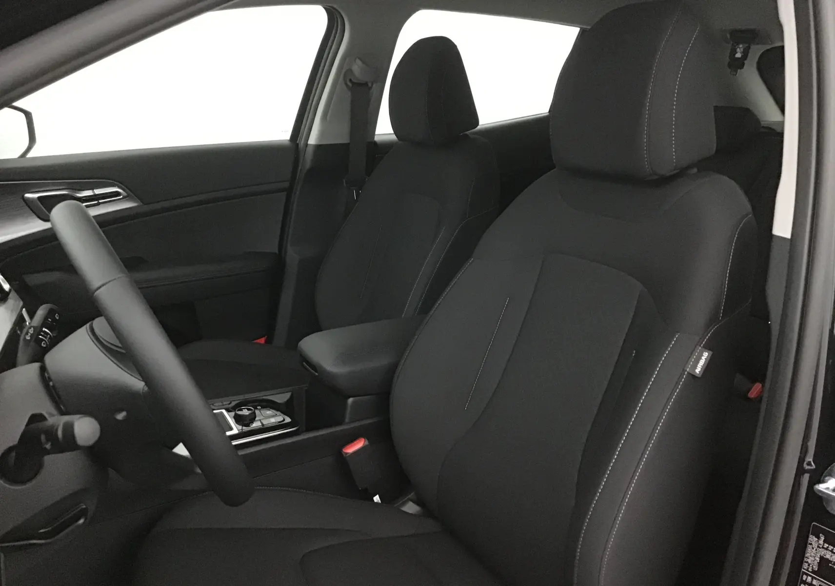 Vue intérieure du côté conducteur du Kia Sportage noir 2025, mettant en valeur les sièges avant en tissu avec coutures contrastées.