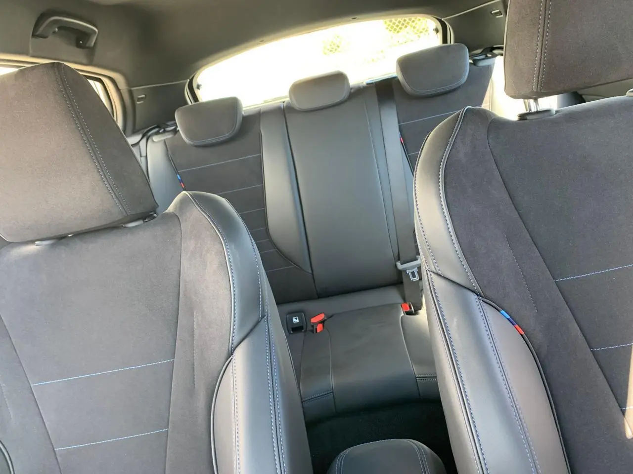 Intérieur de la BMW Série 1 118D M Sport 2025, vue arrière sur les sièges sport en Alcantara noir avec surpiqûres bleues.