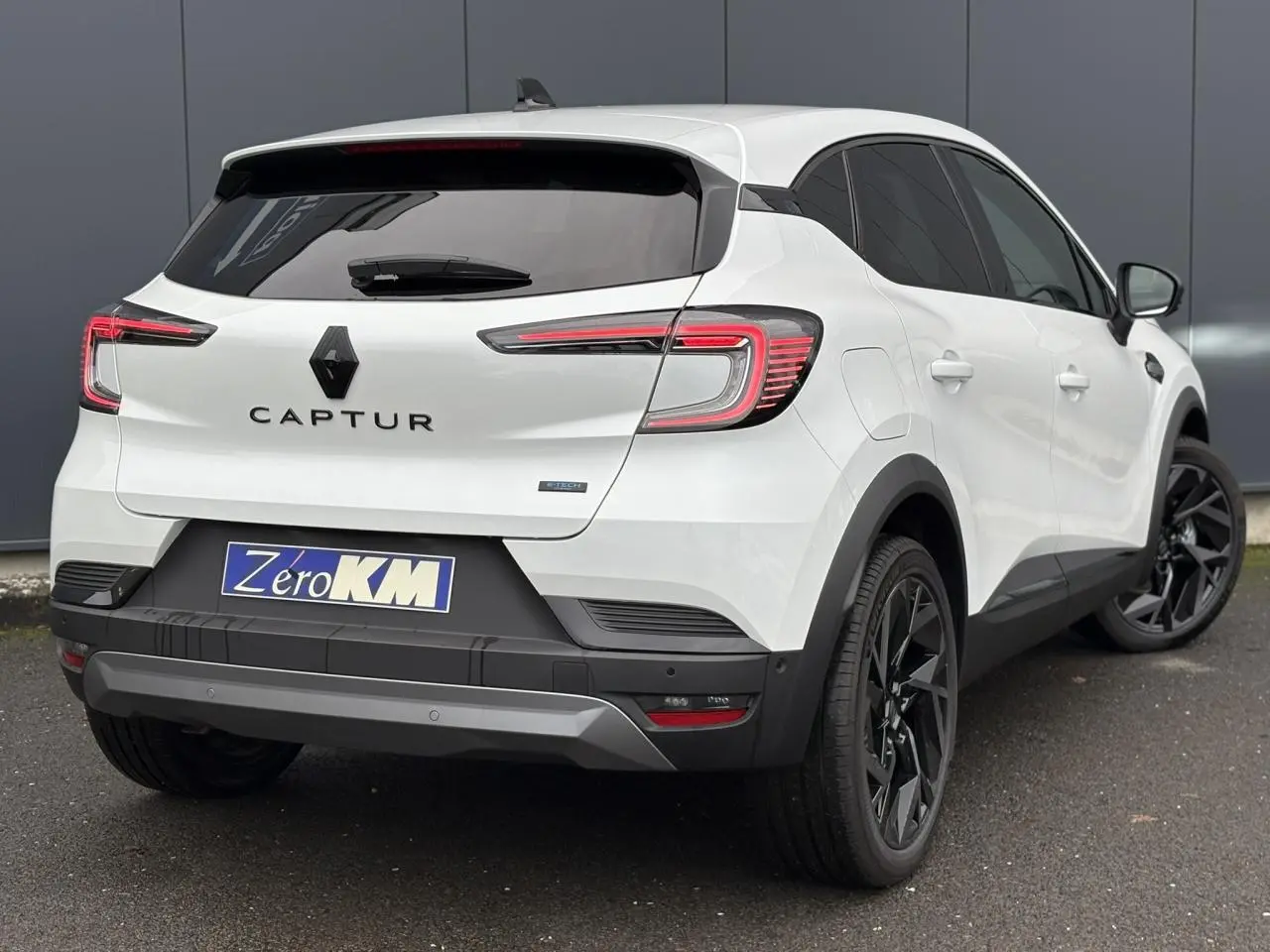 Vue 3/4 arrière droite du Renault Captur blanc nacré avec jantes noires et badge E-Tech sur la malle arrière.