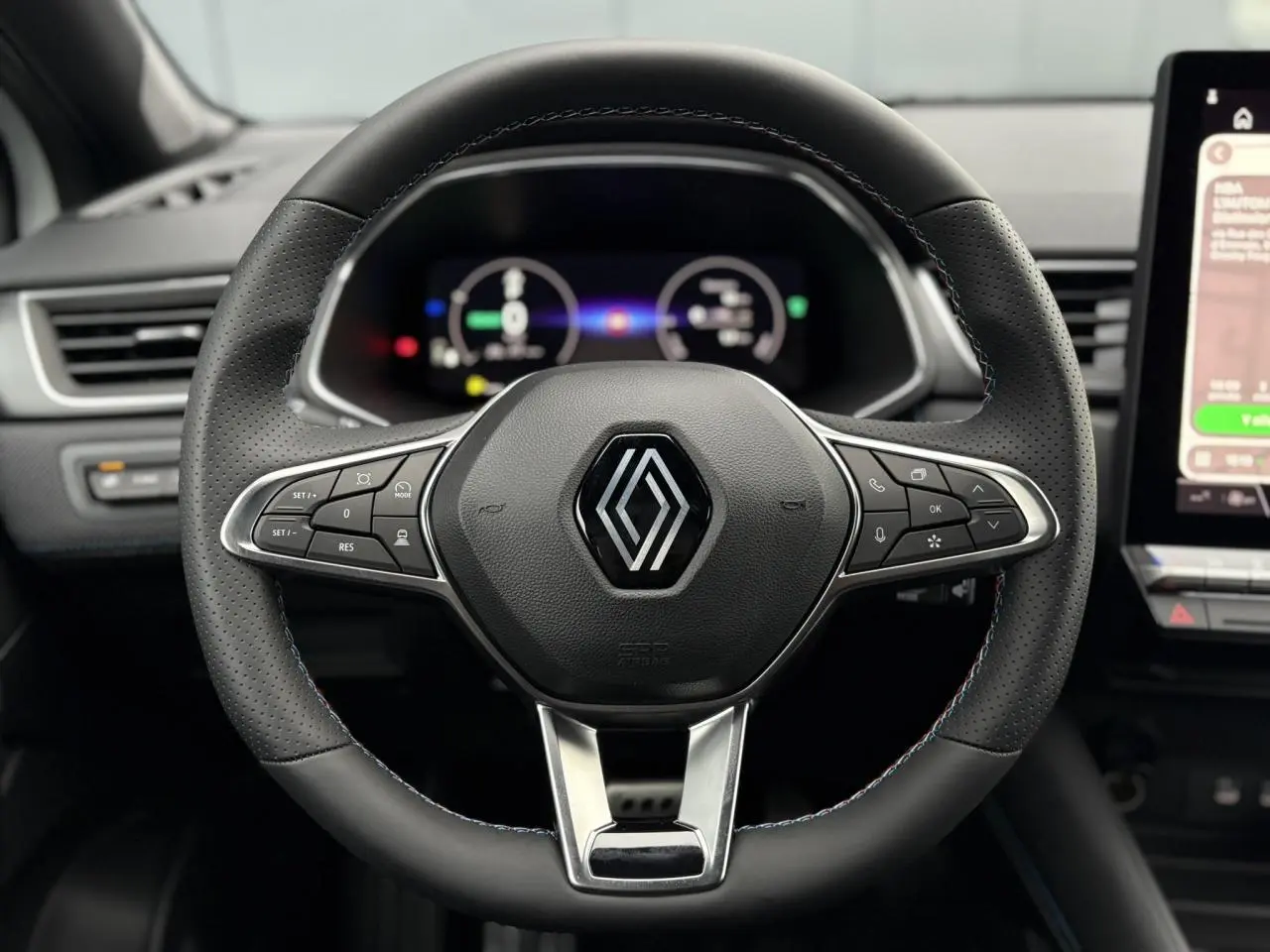 Volant noir perforé avec logo Renault, vue frontale sur tableau de bord numérique et écran tactile latéral.