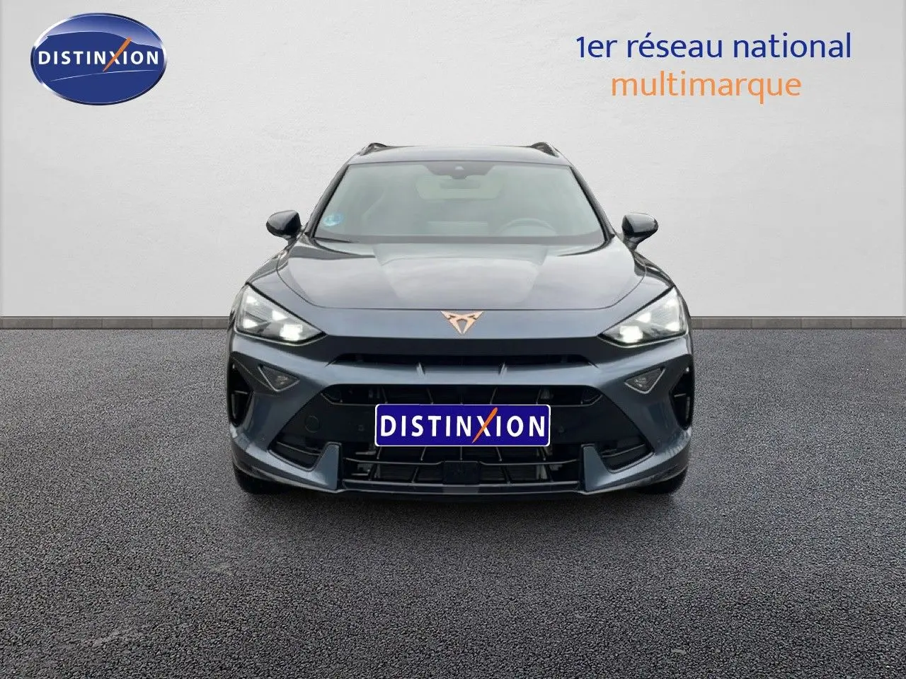 Vue frontale d'un CUPRA Formentor gris magnétique métallisé avec logo cuivré et phares LED allumés.