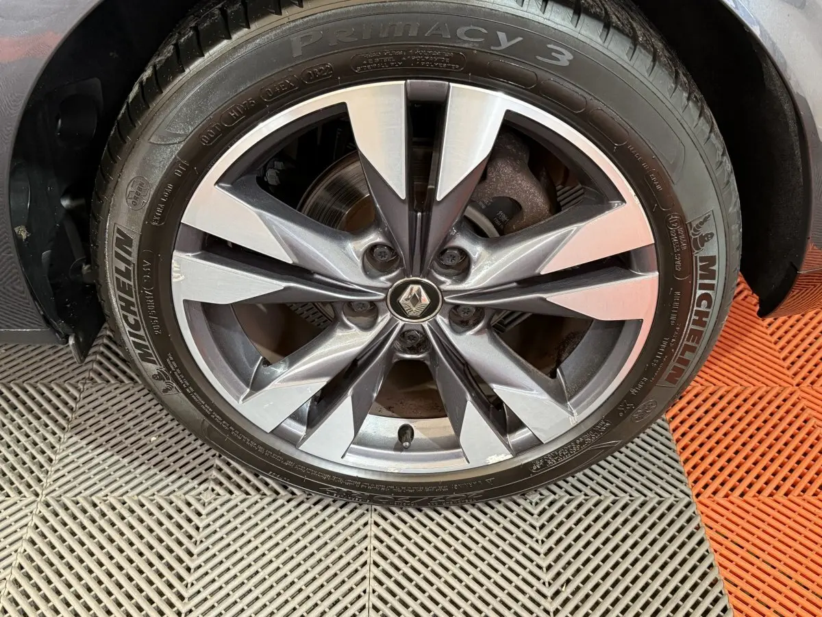 Gros plan sur la roue avant droite de la Renault Mégane gris foncé, avec jante alliage à design moderne et logo Renault central.