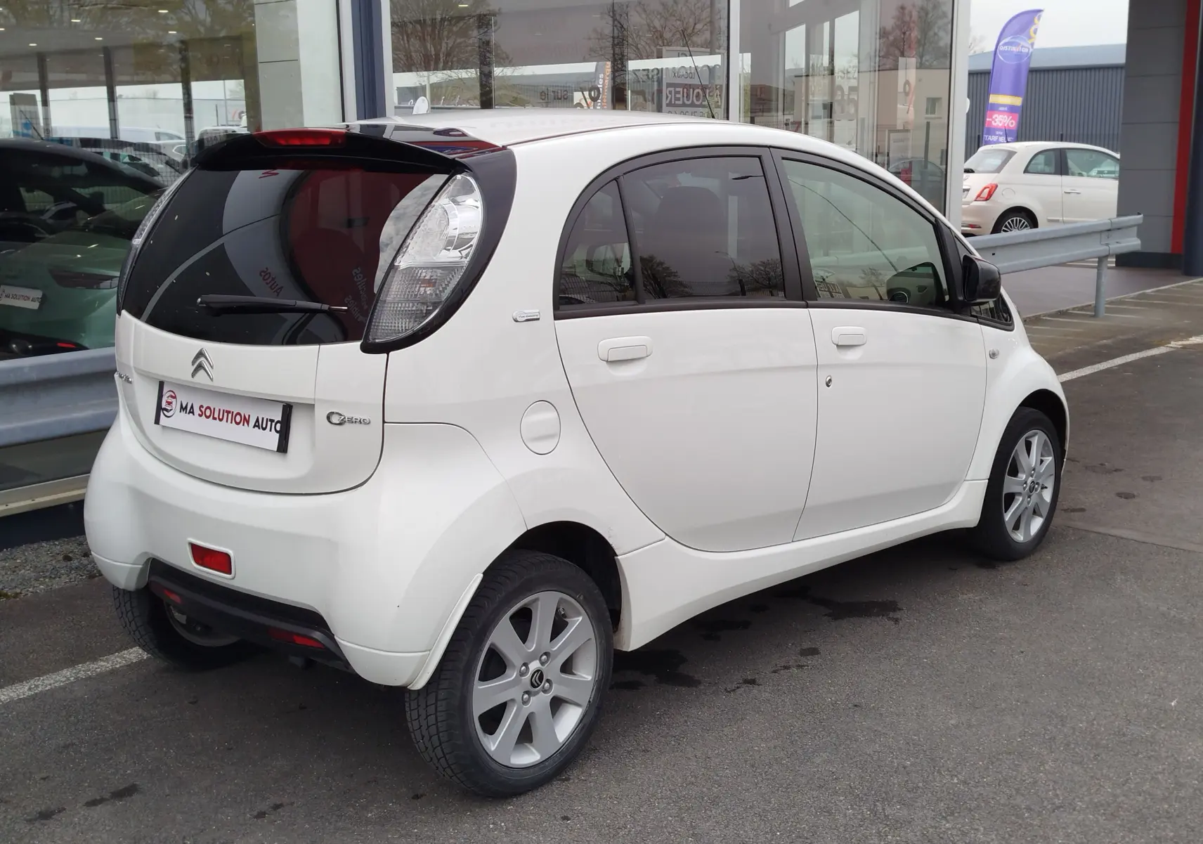 Vue 3/4 arrière droite d'une Citroën C-Zero blanche Antarctique avec vitres teintées et jantes alliage 15 pouces.