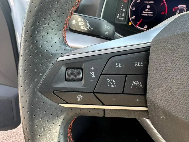 Gros plan sur les commandes au volant perforé avec surpiqûres rouges du SEAT Arona 2025, affichage numérique en arrière-plan.