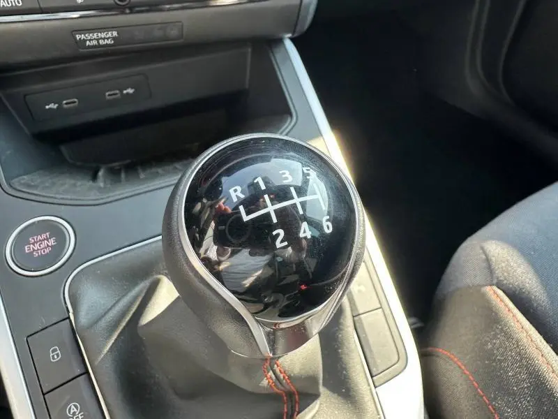 Gros plan sur le levier de vitesses manuel noir avec surpiqûres rouges dans l'habitacle du SEAT Arona blanc toit noir.