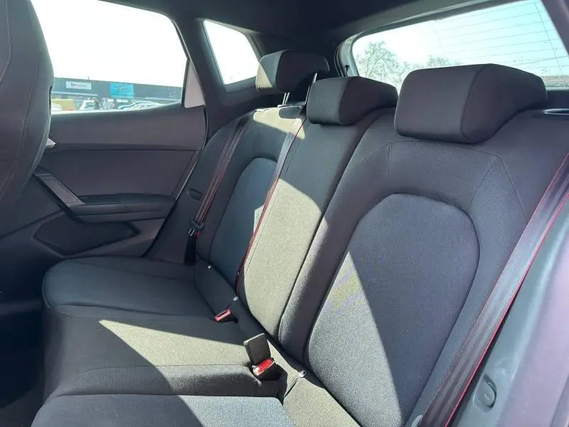 Vue intérieure des sièges arrière du SEAT Arona 2025, tissu noir avec surpiqûres rouges, lumière naturelle entrant par la vitre.
