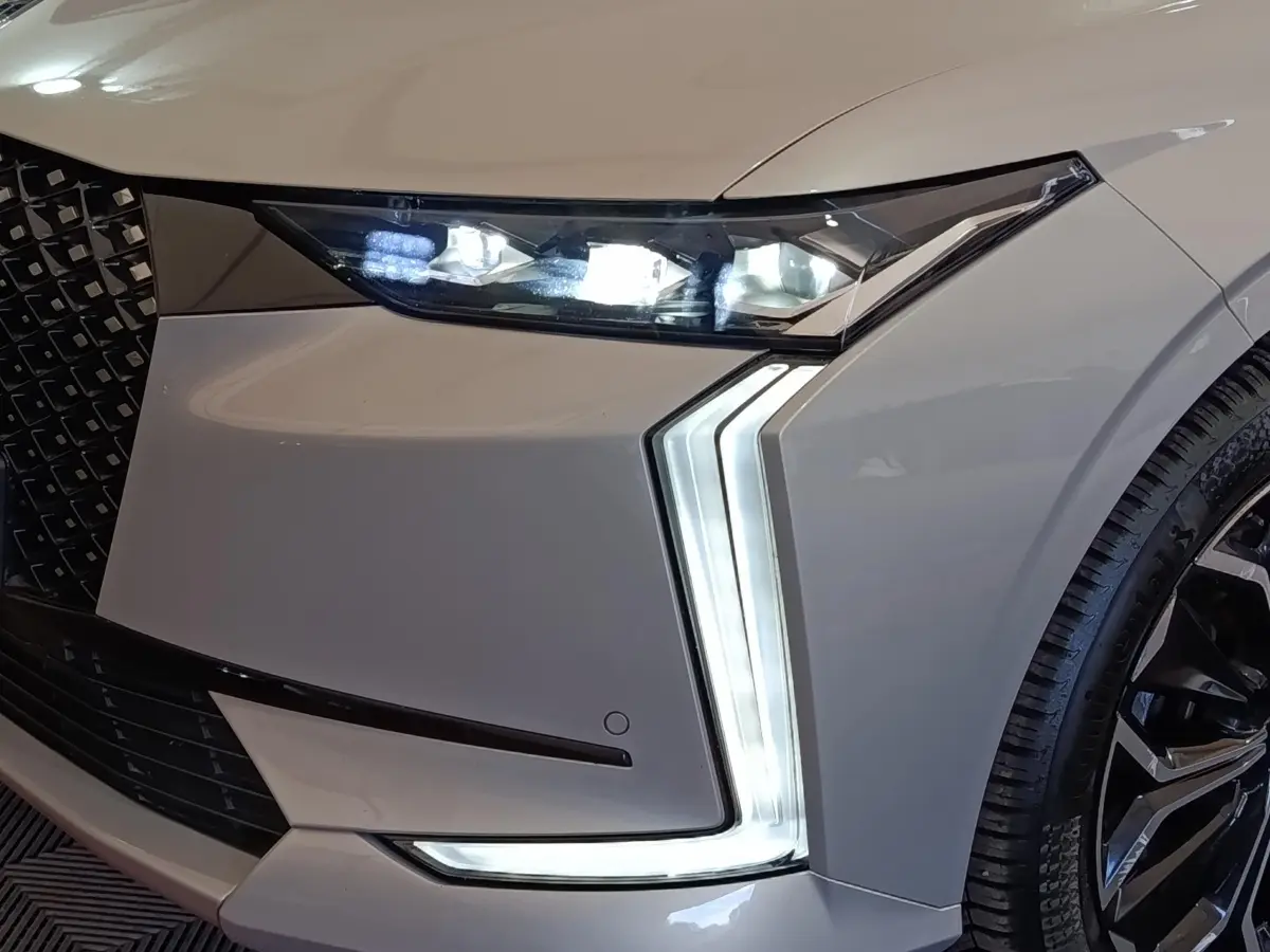 Gros plan sur l'avant droit gris clair du DS4 E-TENSE 225 avec phares LED et feux diurnes en forme de flèche.