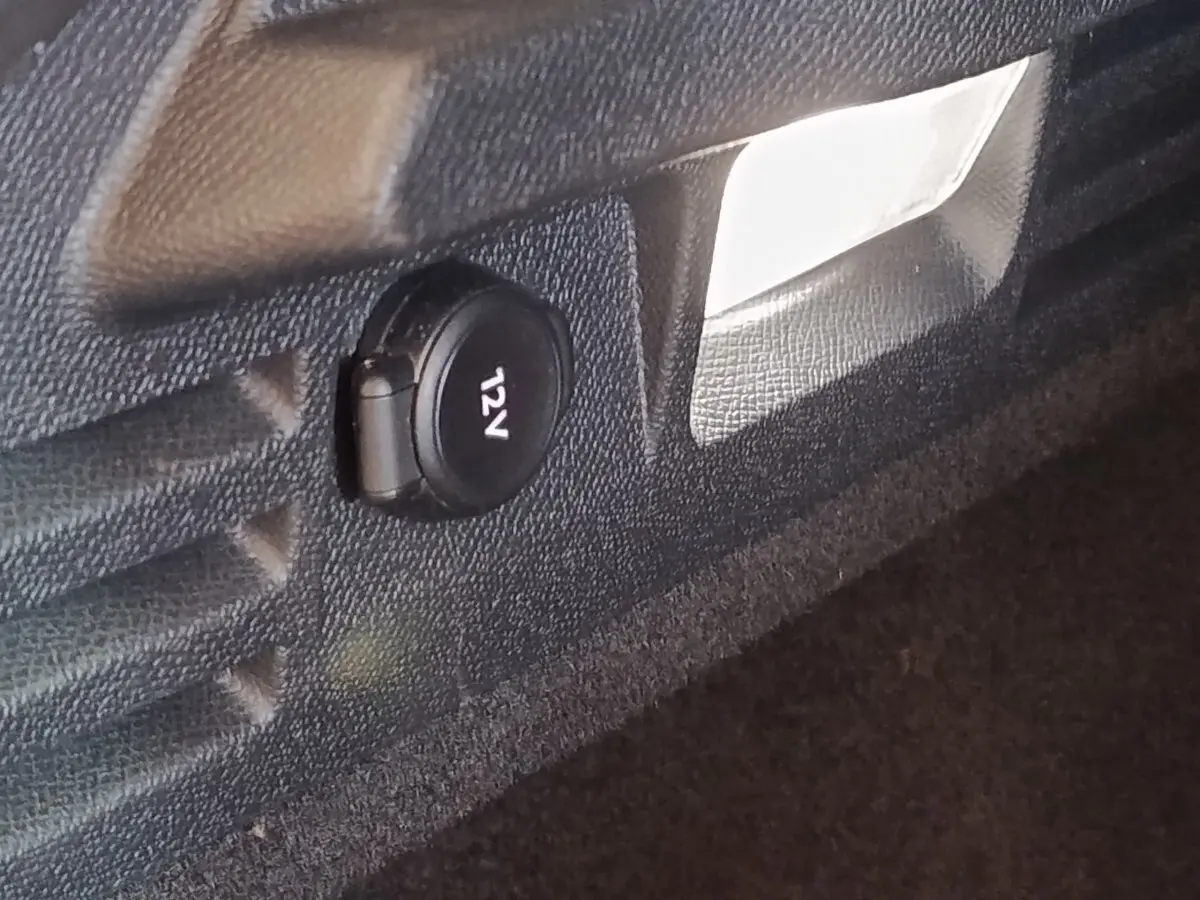 Prise 12V noire dans le coffre du DS4 E-TENSE 225 LA PREMIERE 2021, vue rapprochée sur revêtement noir.