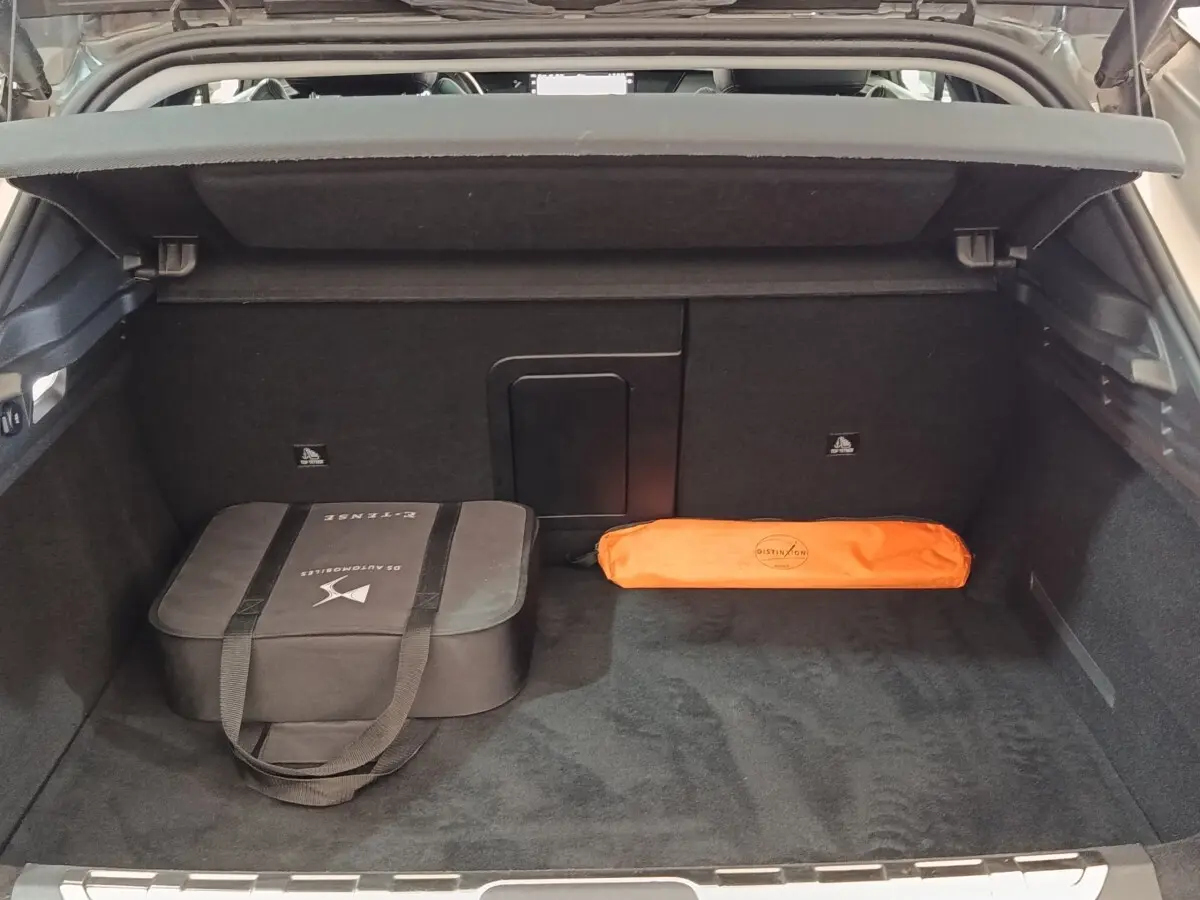 Coffre ouvert d'une DS4 E-TENSE 225 gris clair, montrant un sac noir et une trousse orange rangés à l'intérieur.