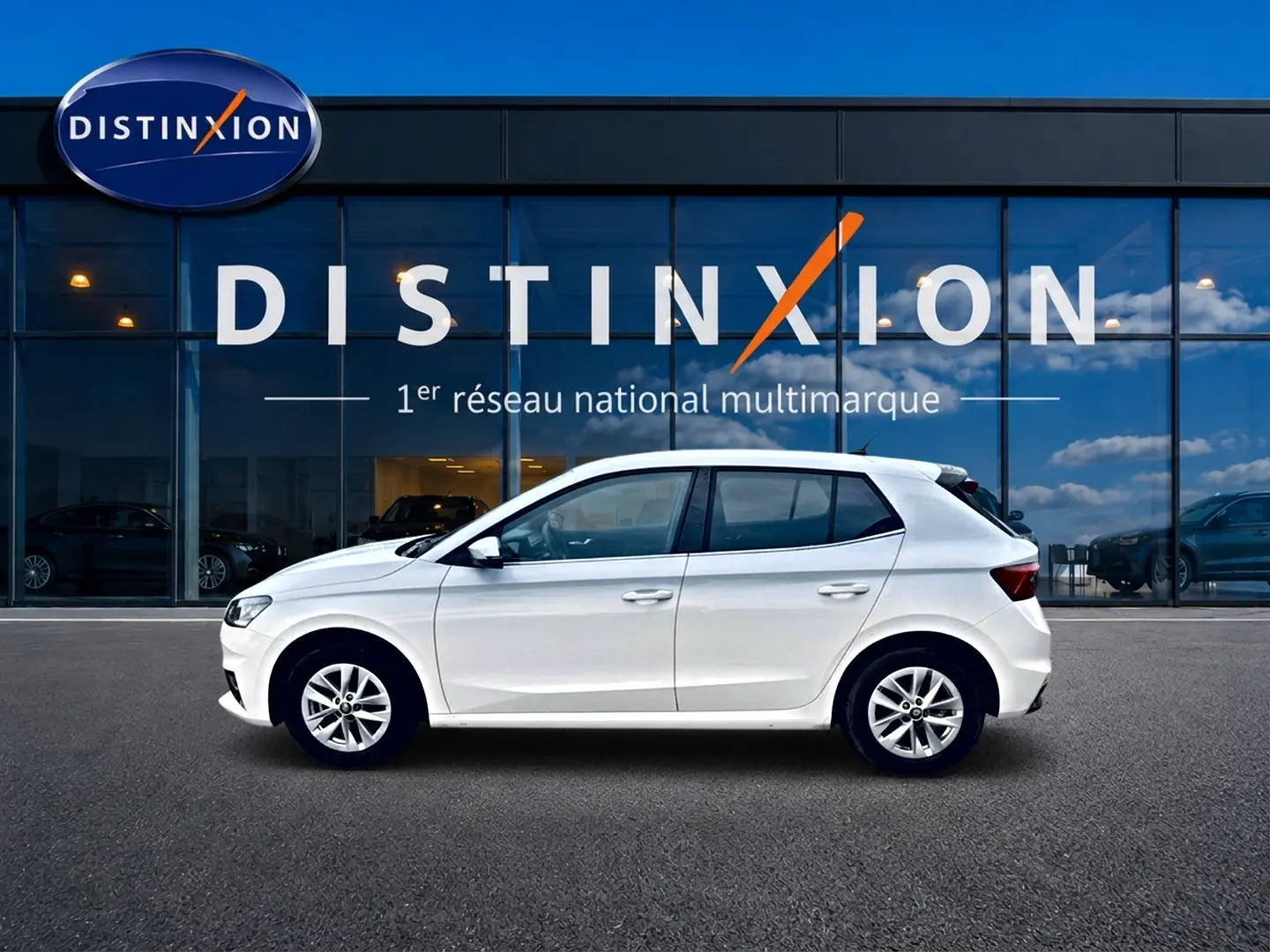 Vue latérale droite d'une Skoda Fabia blanche 2025 garée devant une vitrine avec logo Distinxion.