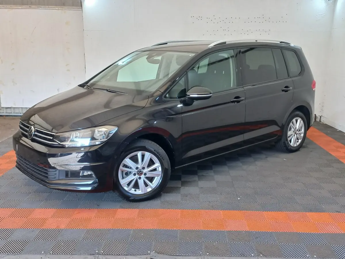 Volkswagen Touran noir vu en 3/4 avant droit, avec jantes alliage et barres de toit chromées visibles.
