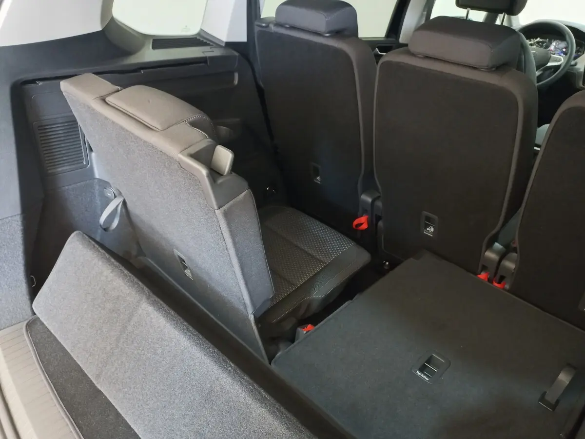 Vue intérieure arrière du Volkswagen Touran 2024 noir, montrant la troisième rangée de sièges partiellement relevée.