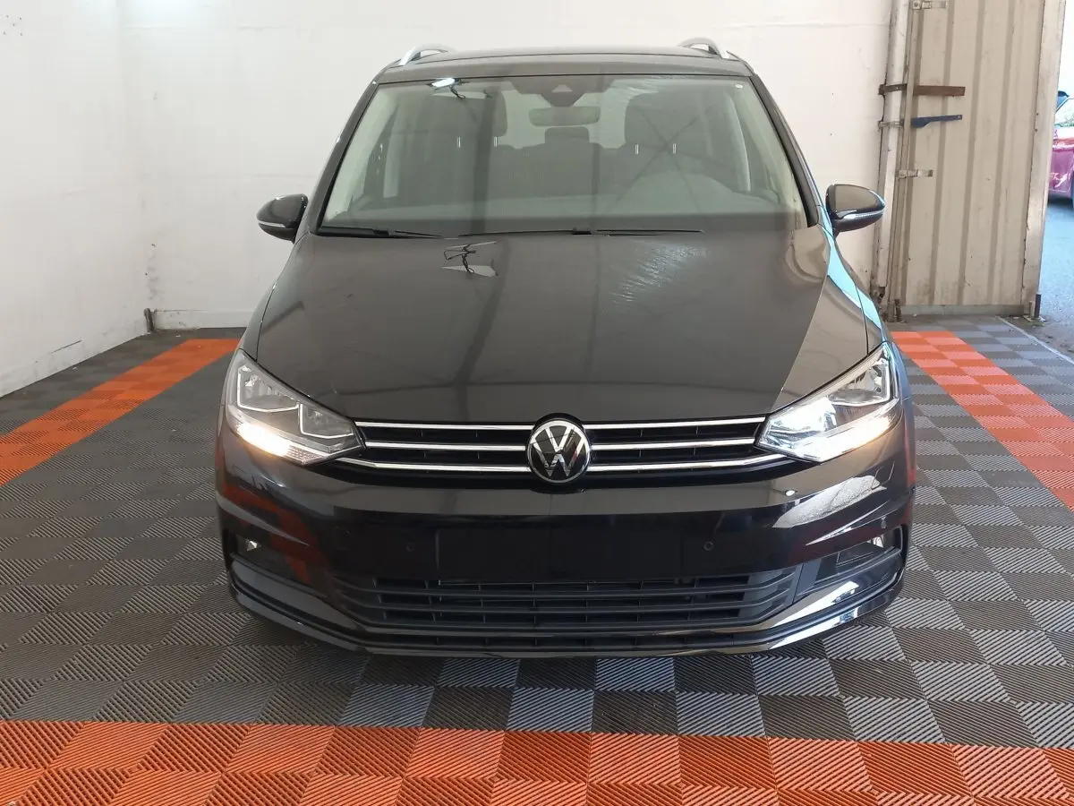 Vue frontale d'un Volkswagen Touran noir 2024 avec phares allumés dans un garage intérieur.