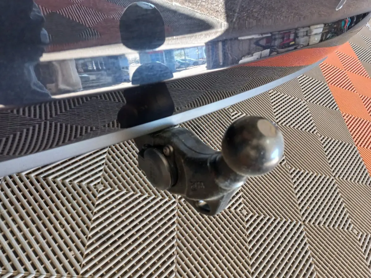 Gros plan sur l'attelage noir fixé à l'arrière d'un Volkswagen Touran noir, avec sol en damier gris et orange.